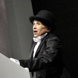 A man in a black tux with a white tie and black top hat stands with his face in shock.