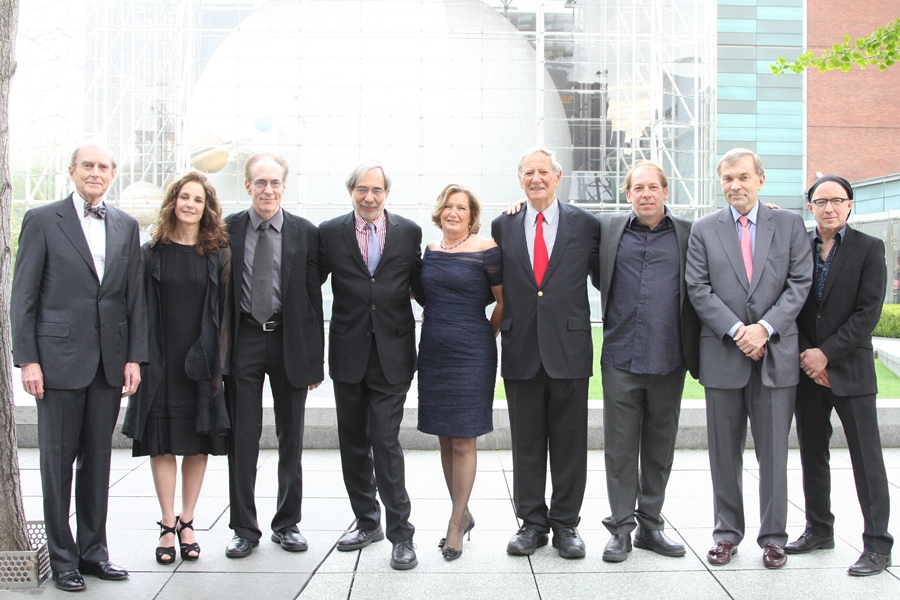 A group of people in dresses and suits stand smiling