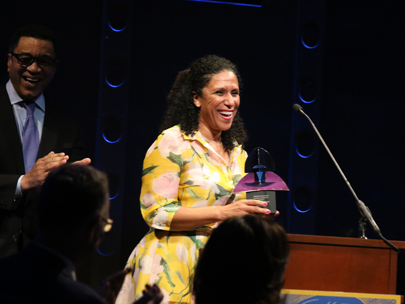 A woman stands smiling holding a award at a podium