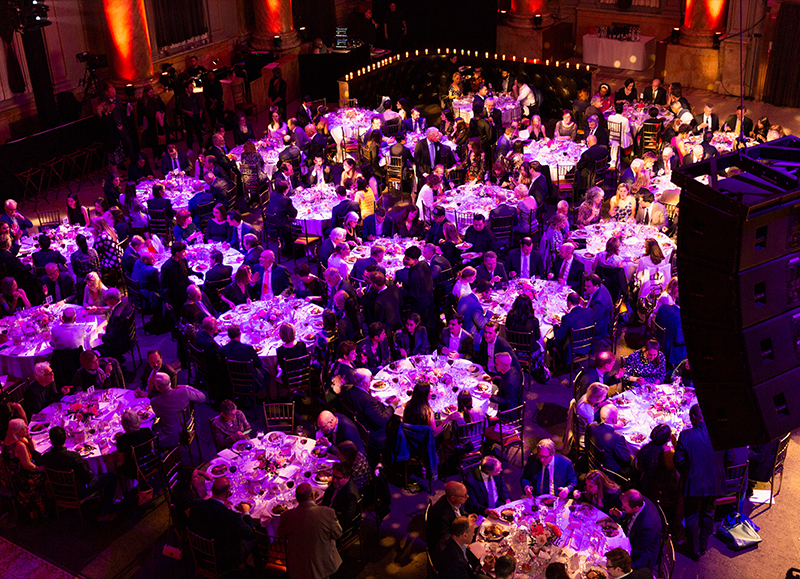An areal view of a huge dance floor filled with dinning room tables and everyone enjoying a meal