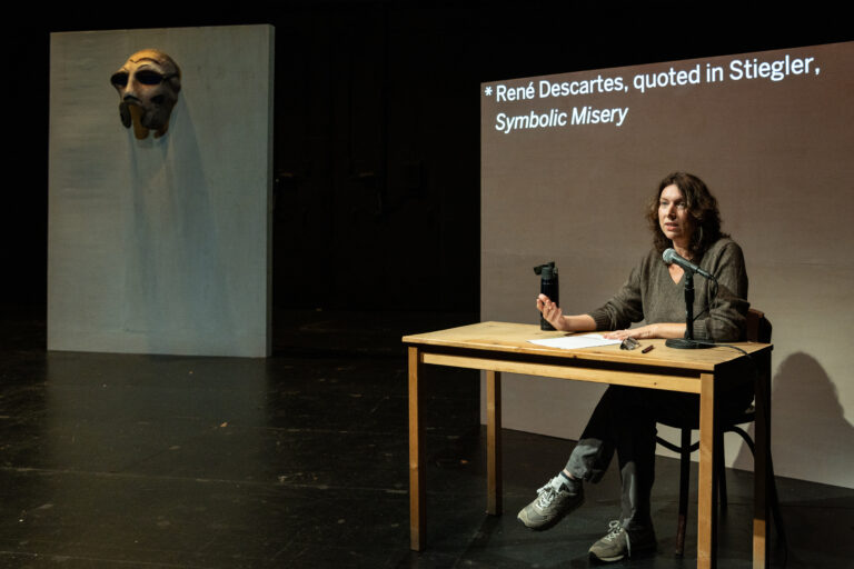 A woman sits at a desk with a microphone answering questions.